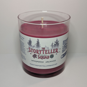 A photo of a glass tumbler with a bamboo lid containing a 10 oz soy wax candle with a short wick. The candle wax is dark maroon in color, and a white label on the glass lists the scent notes, a short section of copy about the candle's scent profile, a QR code, website address, and logo for The Storyteller Squad, and the name of the candle, all in front of the silhouettes of a group of evergreen trees.