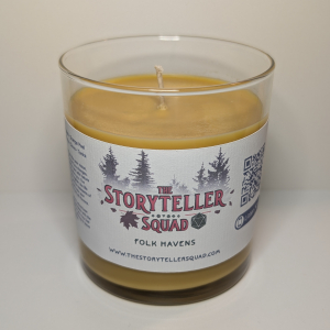 A photo of a glass tumbler with a bamboo lid containing a 10 oz soy wax candle with a short wick. The candle wax is warm yellow in color, and a white label on the glass lists the scent notes, a short section of copy about the candle's scent profile, a QR code, website address, and logo for The Storyteller Squad, and the name of the candle, all in front of the silhouettes of a group of evergreen trees.